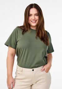 Olivengrøn bomulds t-shirt med klassisk rund hals og korte ærmer, parret med lyse beige bukser med en frontlomme.