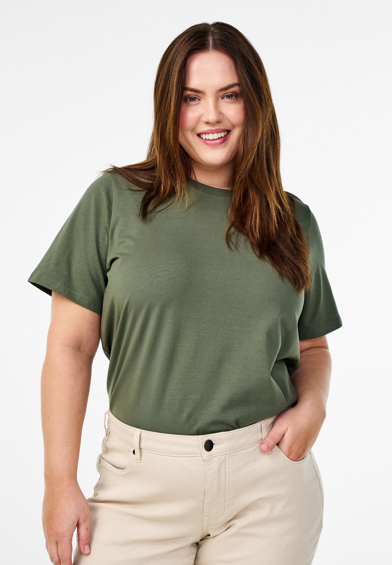 Olivengrøn bomulds t-shirt med klassisk rund hals og korte ærmer, parret med lyse beige bukser med en frontlomme.