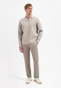 Lichtbeige gebreide pullover met een kraag, gecombineerd met lichtbeige broeken en witte sneakers. Soepele textuur en eenvoudig ontwerp.