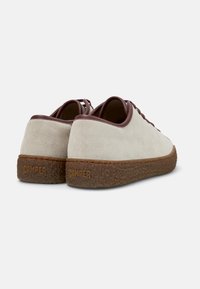 Beige suede sneakers with dark brown accents and textured rubber outsole. Logo embossed on the heel. Classic lace-up design.