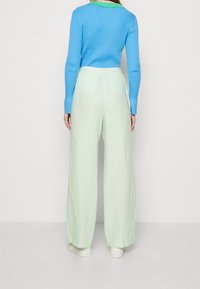 Pantalon large vert clair en lin, accompagné d'un pull côtelé bleu avec un col vert. Silhouette simple et décontractée.