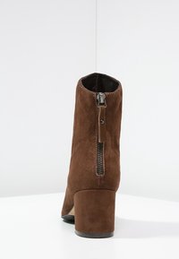 Braune Wildleder-Stiefelette mit Blockabsatz, seitlichem Reißverschluss und glattem Innenfutter. Die Textur ist weich und matt.