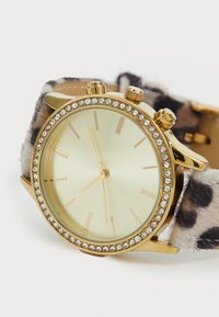 Goldfarbene Uhr mit kristallbesetzter Lünette und Leopardenfell-Armband, die die Uhrzeit 11:00 anzeigt und drei Druckknöpfe an der Seite hat.