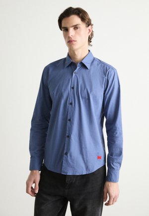 Blue long-sleeve button-up shirt, cotton fabric, classic collar, black buttons, curved hem, red logo tag at the bottom left.