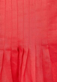 Roter Stoff mit weicher Textur, der vertikale Falten und ein leichtes Finish aufweist. Das Material wirkt glatt und hat eine leicht durchscheinende Qualität.