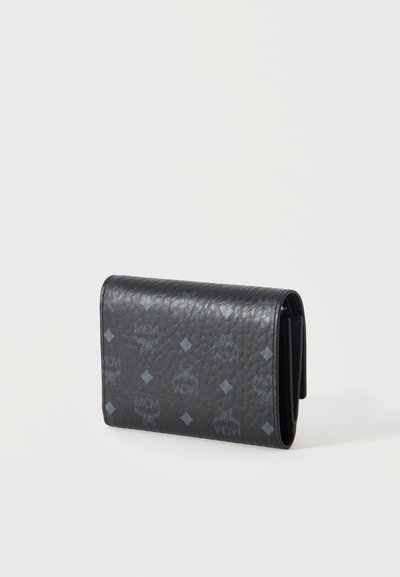 Portefeuille en cuir noir texturé avec logos MCM bleus et formes en losange, plié et posé debout sur un fond clair uni.
