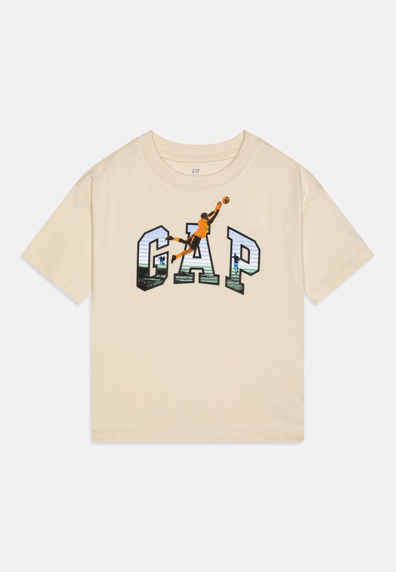 Cream-colored short-sleeve t-shirt with a graphic design featuring the word "GAP" in bold letters and a player in mid-jump with a ball.