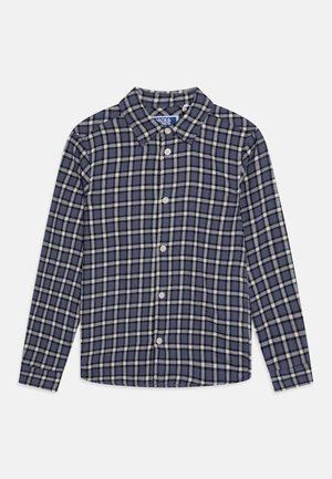 Chemise à manches longues boutonnée, à motif à carreaux bleu et blanc avec un col pointu, posée à plat sur un fond blanc.