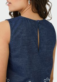 Top senza maniche blu navy con un'apertura a goccia sul retro, caratterizzato da accenti circolari bianchi ricamati all'orlo e un tessuto testurizzato.