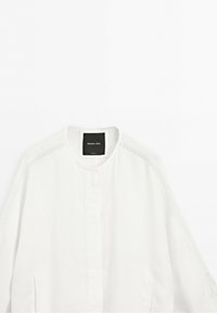 White long-sleeve blouse with round collar and lace detailing along shoulders and sleeves, labeled Massimo Dutti.