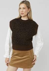 Pull en imprimé léopard marron avec un col et un ourlet côtelés, porté sur un haut à manches longues en dentelle blanche. Associé à une jupe en velours côtelé marron.