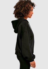 Sudadera negra con un corte holgado, bolsillos frontales, capucha con cordón y puños acanalados. Fabricada en una suave mezcla de algodón con textura lisa.