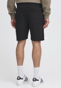 Shorts en coton noir présentant un design simple, avec une unique poche arrière et une ceinture élastique. Portés avec des chaussettes blanches et des baskets.