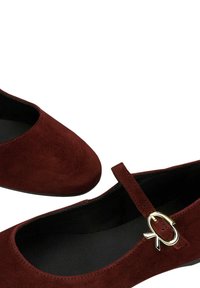 Scarpe Mary Jane basse in suede rosso scuro con fibbia dorata e fodera interna nera su sfondo bianco.