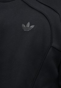 Μαύρο φούτερ με διακριτικό μαύρο λογότυπο Adidas trefoil στο στήθος και ορατές ραφές στην περιοχή των ώμων.