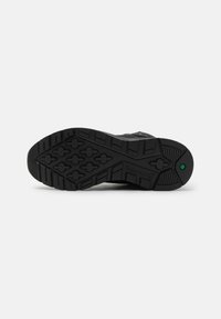Suela de zapato de goma negra con un patrón de relieve profundo, que presenta formas hexagonales y en cruz para una mejor tracción. Superficie texturizada con la marca Timberland.