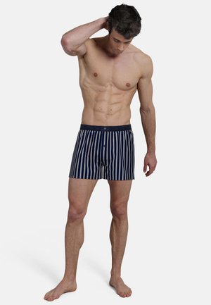 Navy blue swim shorts with white vertical stripes, elastic waistband, and a button detail on the front. Made from lightweight fabric.