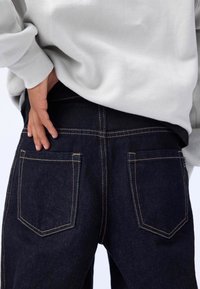 Dark denim jeans with an elastic waistband, highlighted by contrasting yellow stitching and two back pockets with a classic design.