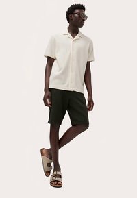 Lysebeige kortærmet ribbet skjorte, mørkegrønne shorts og beige sandaler med justerbare stropper. Glatte teksturer, afslappet pasform.