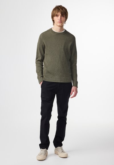 Maglione verde oliva con texture a costine, scollatura rotonda, abbinato a pantaloni neri e sneaker beige chiaro. Design semplice e casual.