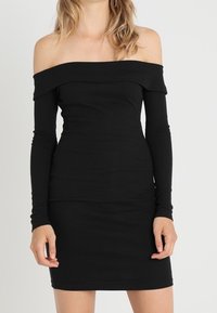 Černé šaty na jedno rameno vyrobené z ribbového materiálu; přiléhavý střih s dlouhými rukávy a délkou ke kolenům.