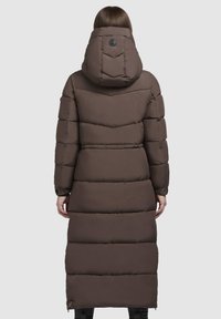 Lange bruine pufferjas met een capuchon, voorzien van een chevron-quiltpatroon, een taille die kan worden aangesnoerd en zijzakken met rits. Glad, gepolsterde textuur.