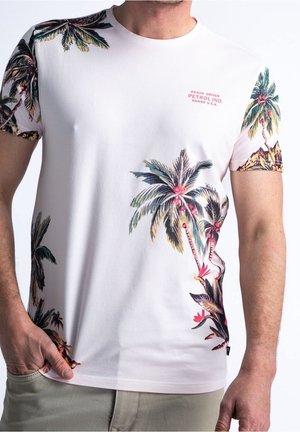 Weißes Kurzarm-T-Shirt mit bunten Palmen- und tropischen Blumenmotiven auf den Ärmeln und vorne, getragen von einer Person mit der Hand in der Tasche.