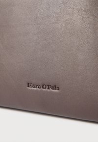 Prim-plan al unei suprafețe netede din piele gri, cu numele mărcii „Marc O’Polo” imprimat în litere întunecate.