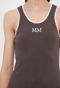 Dunkelbraunes, geripptes Tanktop mit weißen Akzenten. Auf der Vorderseite sind die gestickten Initialen "MM" deutlich sichtbar.