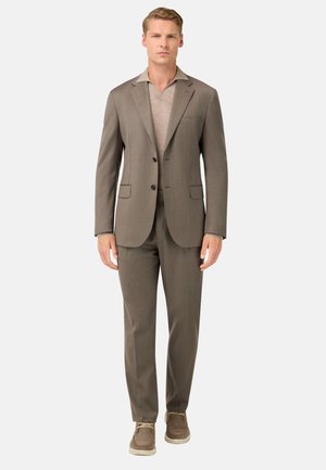 Costume marron sur mesure avec un revers en pointe, deux boutons et des poches latérales, associé à un polo beige clair et des chaussures marron clair.