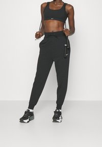 Svart sport-bh och joggers med dragsko i midjan, tillverkade av texturerad tyg. Komplett med svarta och vita träningsskor.