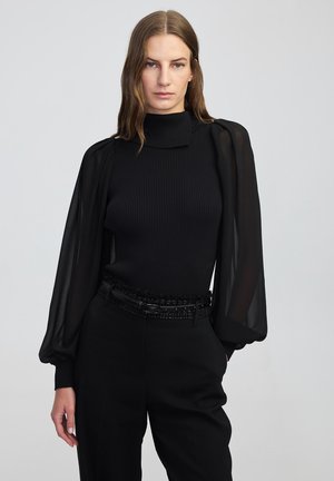 Top lungo a maniche ribbed nere con maniche puff trasparenti, caratterizzato da un collo alto e una cintura nera texturizzata con decorazioni.
