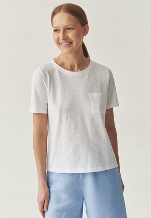Witte t-shirt met korte mouwen en een ronde hals, voorzien van een klein borstzakje. Soepele textuur, gecombineerd met lichtblauwe broek.