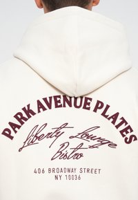 Cream hoodie featuring maroon embroidered text. Design includes "PARK AVENUE PLATES" and "Liberty Lounge Bistro" in cursive.