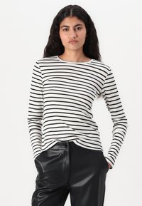 Haut à manches longues en coton côtelé de couleur ivoire avec des rayures horizontales noires, présentant un décolleté arrondi et une coupe ajustée. Associé à un pantalon en cuir noir.