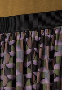 Jupe multicolore avec une section supérieure marron, une taille élastique noir et un tissu en maille à motifs avec des cercles verts, violets et marron.