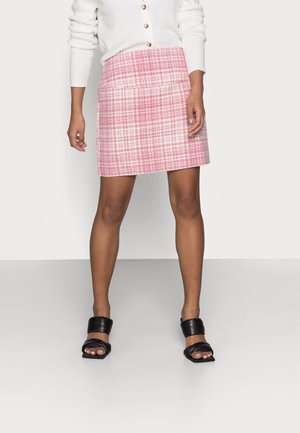 Minifalda de tweed rosa con un patrón de cuadros, diseño estructurado y corte recto, complementada con un cárdigan blanco acanalado y sandalias negras.