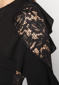 Vestido preto com uma sobreposição de renda nos ombros. O material é suave com um padrão de renda texturizado, criando um efeito em camadas.