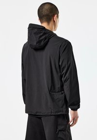 Black hooded jacket made from lightweight fabric, featuring a relaxed fit, adjustable hem, and two side pockets with zippers.