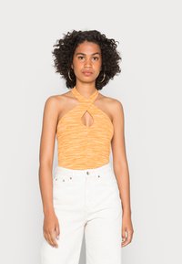 Top de halter em tecido laranja canelado com um detalhe em forma de buraco, combinado com calças brancas de cintura alta. A textura parece suave e elástica.