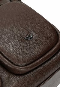 Borsa in pelle marrone con finitura strutturata, bordi arrotondati e un piccolo dettaglio del logo nero sulla patta anteriore.