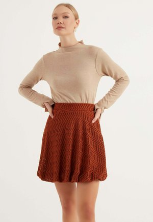 Beige lange mouw top met een hoge halslijn, gecombineerd met een roestkleurige rok met zigzagpatroon, gekenmerkt door een flared vorm en textuurstof.