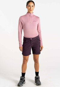 Sudadera de manga larga rosa con cremallera y patrón de rayas texturizadas, combinada con pantalones cortos morados oscuros. Los accesorios incluyen botas de senderismo grises.