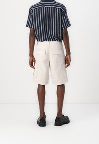 Beige cargoshorts met meerdere zakken, gemaakt van lichtgewicht stof. Gecombineerd met een marineblauw gestreept shirt met korte mouwen en zwarte veter schoenen.
