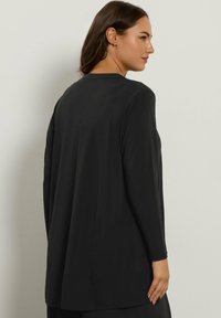 Maglia nera a maniche lunghe realizzata in un materiale liscio, caratterizzata da una vestibilità comoda, scollatura rotonda e orlo posteriore più lungo.