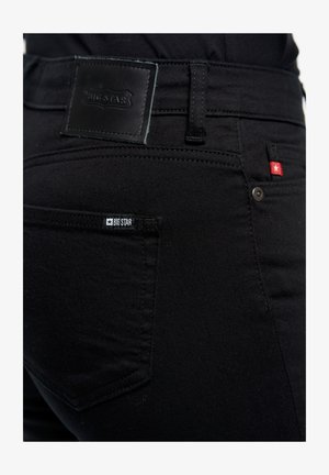 Fekete farmernadrág bőr címkével és egy kis márkajelzéssel. Normál zsebekkel és finom varrási részletekkel készült.