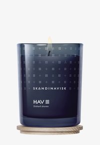 Ett mörkblått ljus i en glasbehållare med ingraverade mönster, med en träbas och en synlig låga. Etiketten lyder "SKANDINAVISK HAV Fjärran stränder."