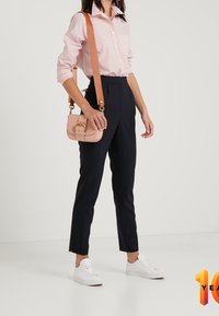 Chemise boutonnée rayée rose clair avec les manches retroussées, pantalon noir ajusté et baskets blanches. Le mannequin porte un petit sac bandoulière rose.
