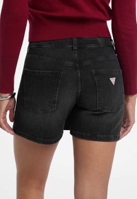 Crne traperice šortse imaju klasičan kroj s stražnjim dzepovima i malim logotipom. Tkanina ima glatku teksturu i blago izbjeljivanje.