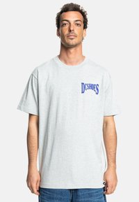 Gray cotton t-shirt with short sleeves, a crew neck, and blue "DCSHOES" logo on the left chest. Relaxed fit and soft texture.